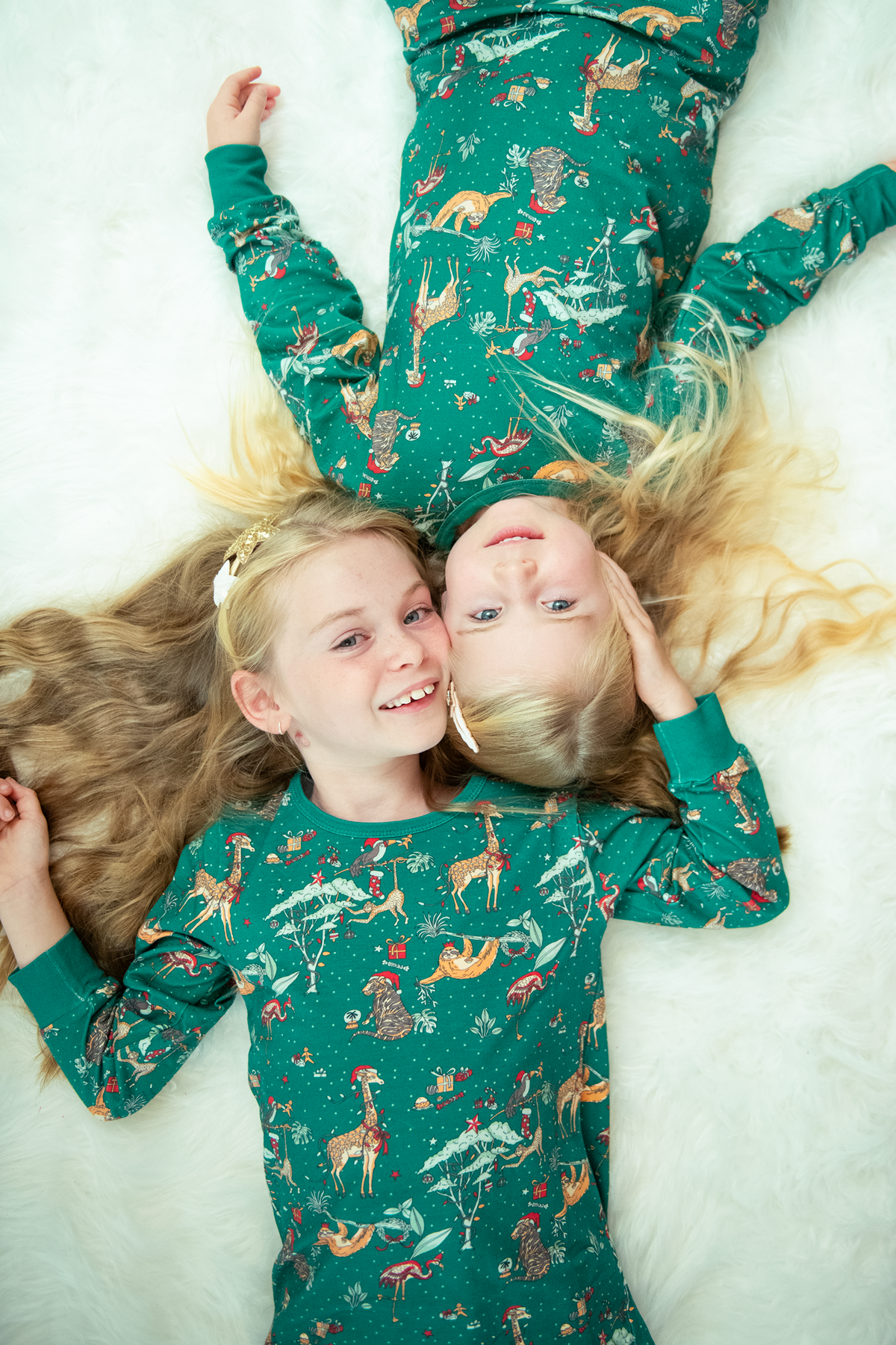 Two children lying on a bed wearing matching green jungle Christmas pyjamas with festive animal print.