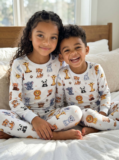 Brother and sister wearing matching white animal print pyjamas sitting together on a bed