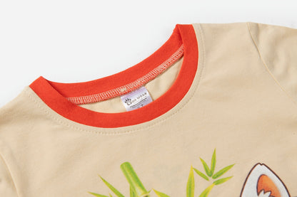Close-up of a beige t-shirt with a contrasting orange-red ribbed crew neck collar, featuring a partial green bamboo and fox graphic at the bottom.