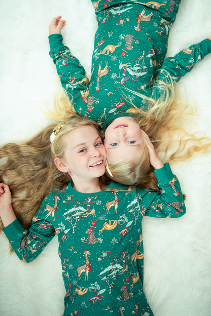 Two children lying on a bed wearing matching green jungle Christmas pyjamas with festive animal print.