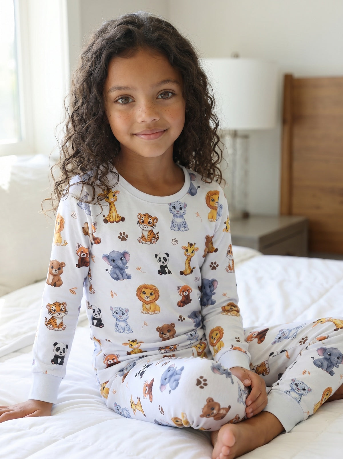 Girl wearing white safari animal print pyjamas sitting on a bed