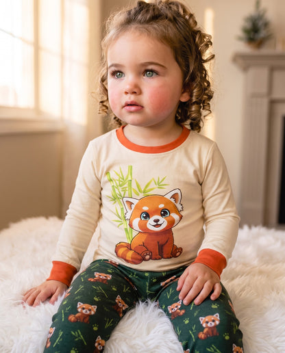 Toddler wearing Red Panda cotton pyjamas sitting on a bed smiling at the camera