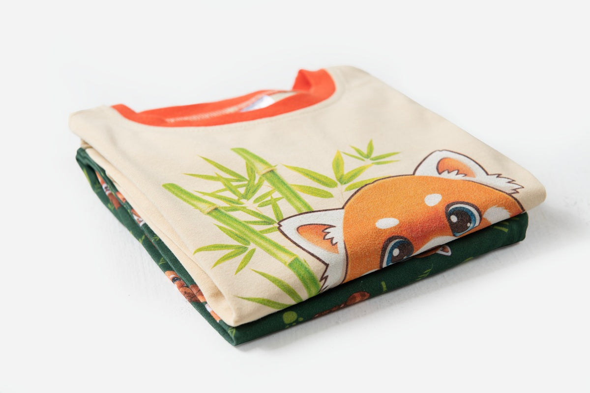 Close up Folded PJs featuring cute red panda illustrations, one in beige with green bamboo and one in dark green with small red panda prints.